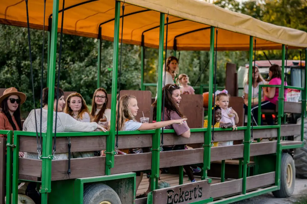 Passengers are seated on a green tram with wooden benches, enjoying a ride outdoors.