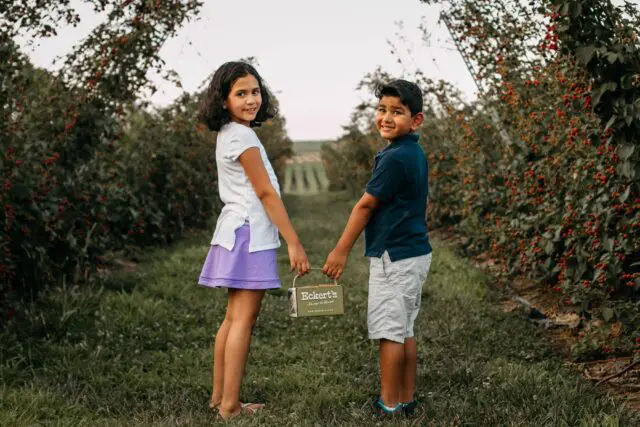 Two children smile holding a sign, standing amidst lush greenery.