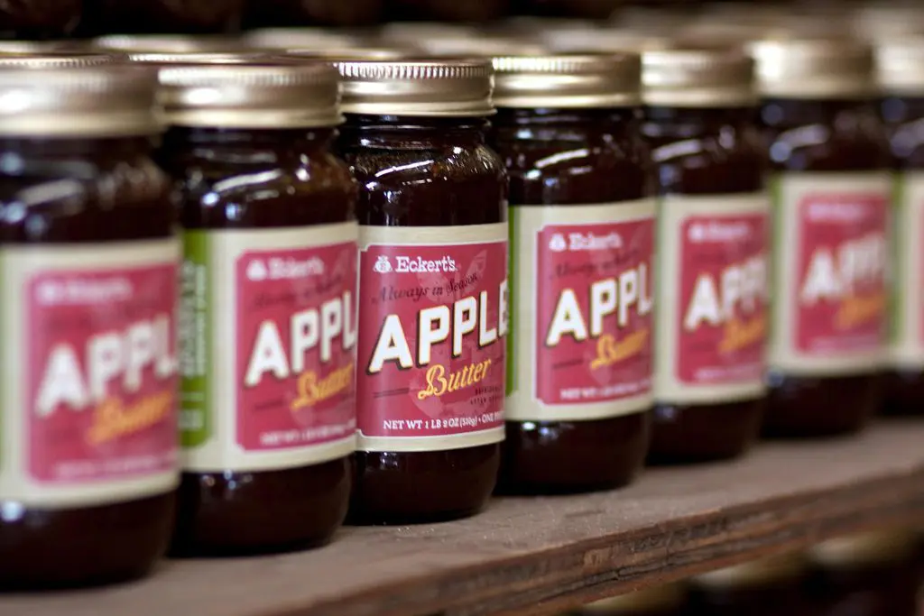 Rows of jars labeled "Apple Butter" are lined up on a wooden shelf, with a focus on one jar in the center.
