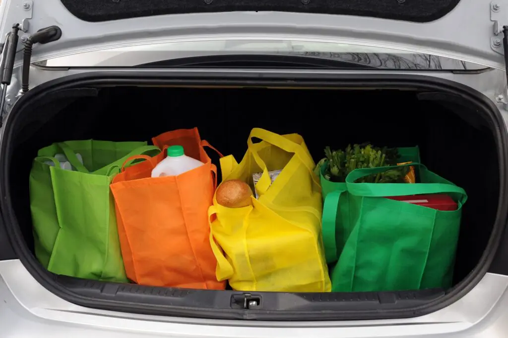 A picture of groceries in the trunk of a car in colorful reusable tote bags.
