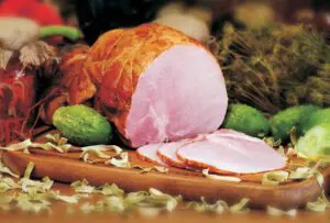 A picture of a sliced ham surrounded by vegetables and ingredients