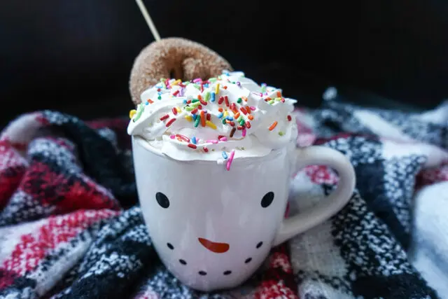 snowman hot cocoa mug with cider donut on plaid blanket
