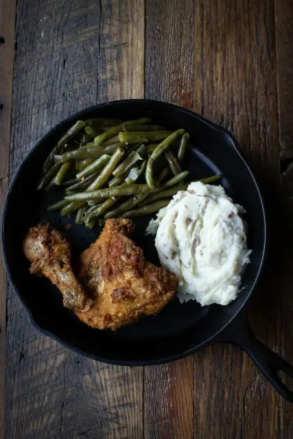 Two pc Fried Chicken skillet with green beans and mashed potatoes served in cast iron style pan.