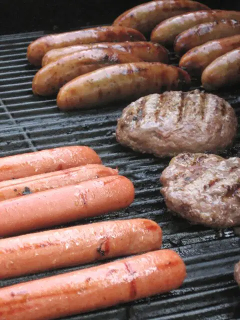 A picture of hotdogs, hamburgers, and bratwurst on a grill