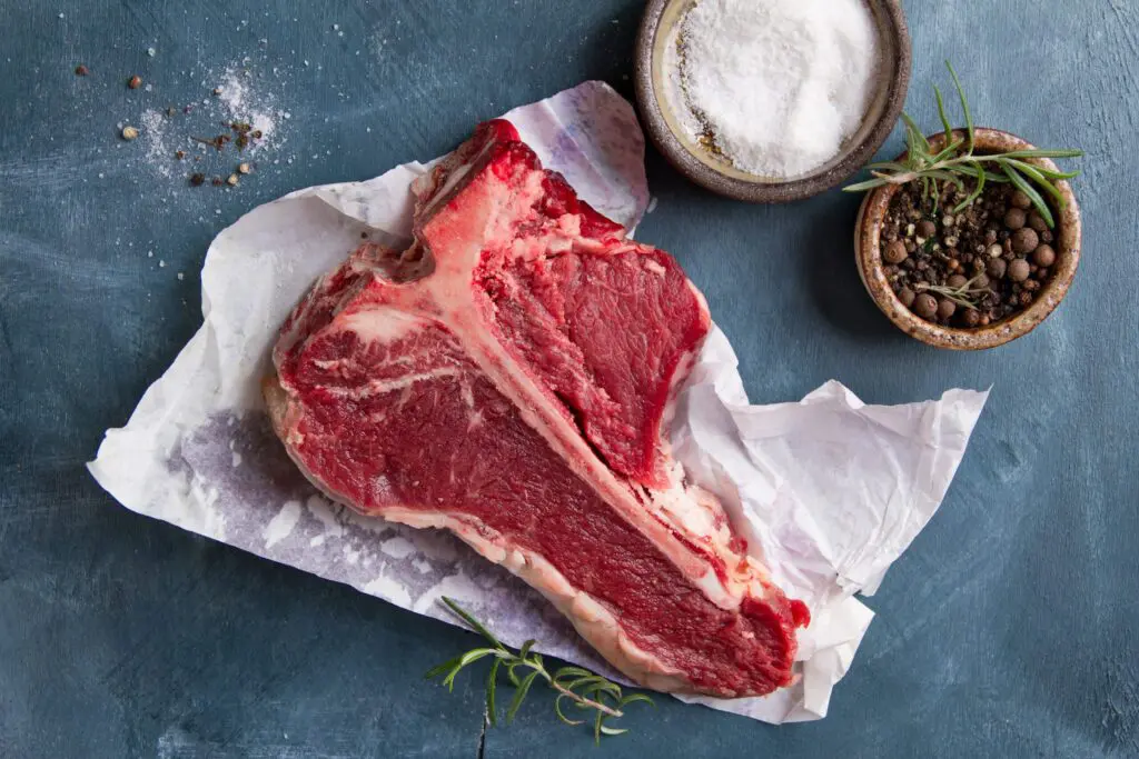A picture of a thick raw T-bone steak with seasoning