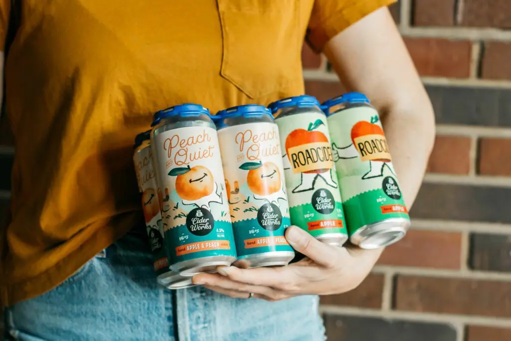 Woman with yellow shirt Holding Eckert's 8 pkg of hard Ciders.