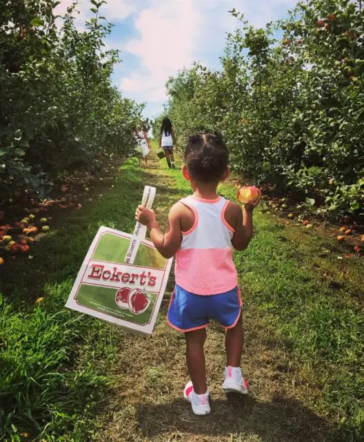 Young girl carrying a peach and an Eckert's bag through an orchard