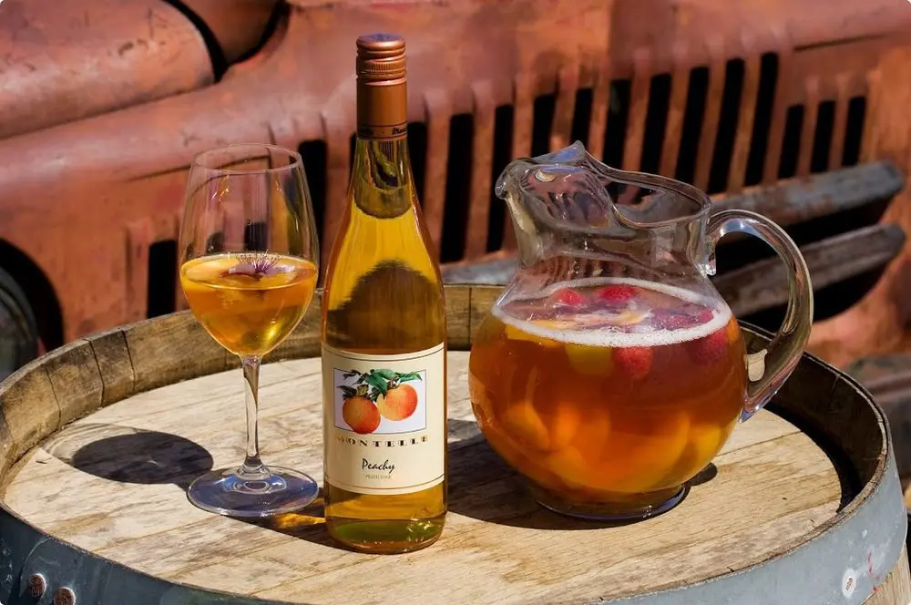 Bottle, Pitcher and Wine Glass of Peachy Sangria served outdoors on barrel top