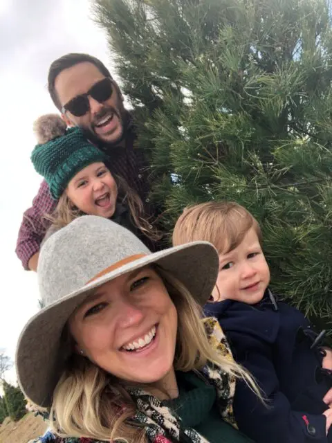 A happy family poses with smiles outdoors, with trees in the background.