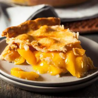 A slice of peach pie with a flaky crust on a plate, demonstrating a delicious homemade dessert.