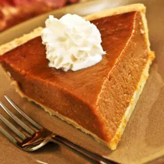 Pumpkin Pie slice on plate with fork and whipped cream.