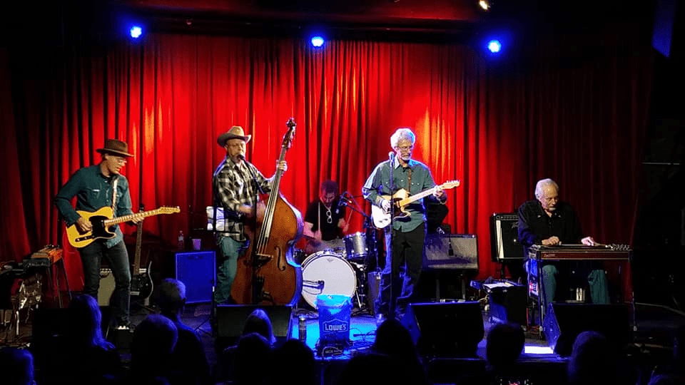 Cider Shed Live Music: Colonel Ford. A band performs on stage with a guitarist, bassist, pianist, and a drummer under red lighting.