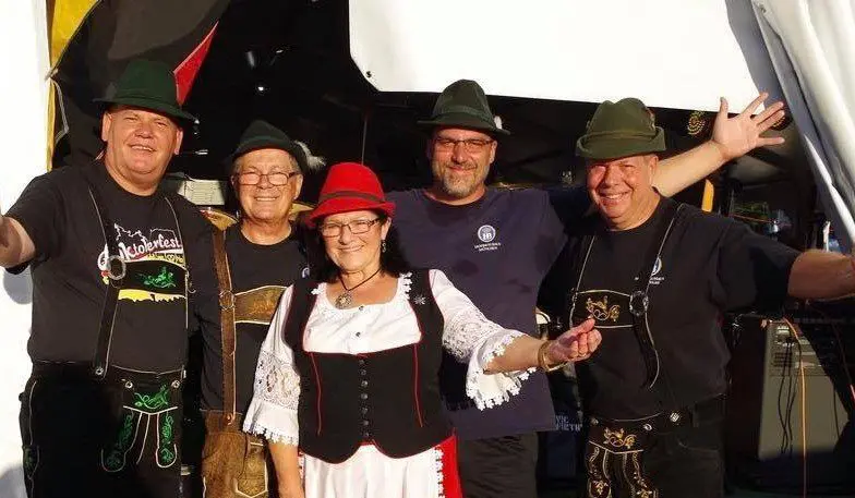 A group wearing traditional German attire smiles cheerfully, possibly at a festive event.