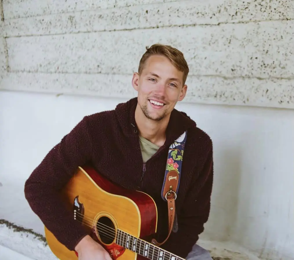 Cider Shed Live Music; Andrew Dahle close up holding guitar in front of white building.