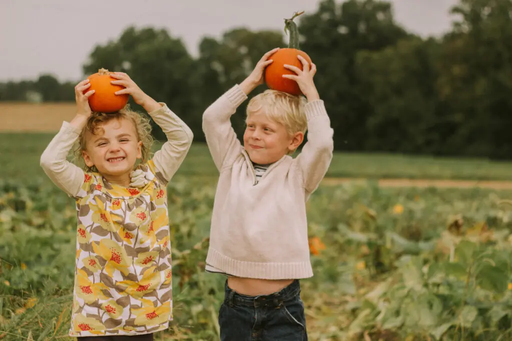 Two children holding pumpkins on their heads. Pumpkin Picking School Tour