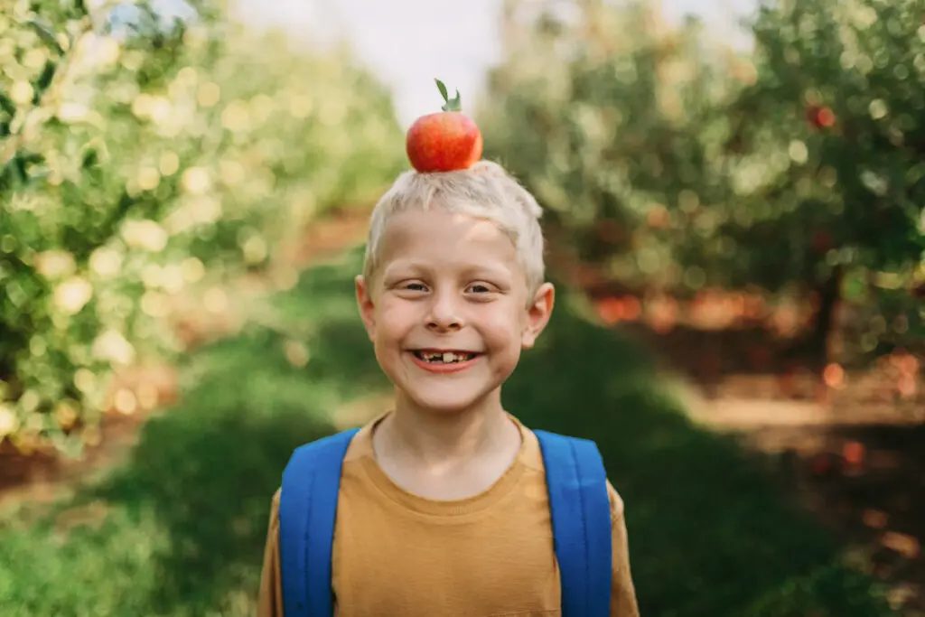 apple farm school tour - little boy with apple on his head in orchard