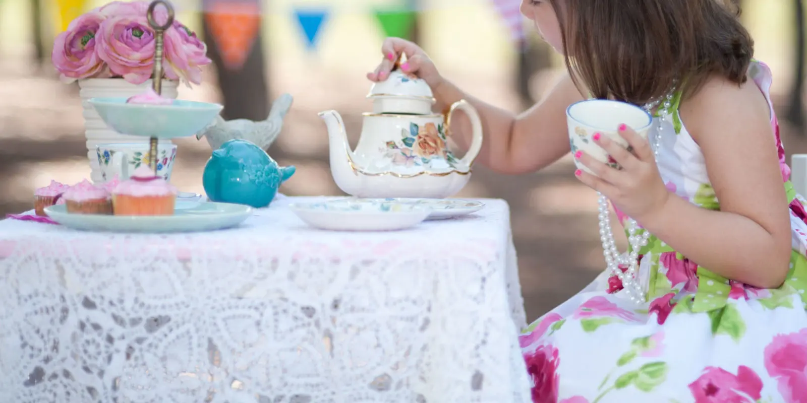 Tea Party. Little Girl with tea pot sitting at table.
