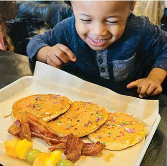 Restaurant Easter Flippity Flop Breakfast; kid with pancakes, bacon, fruit