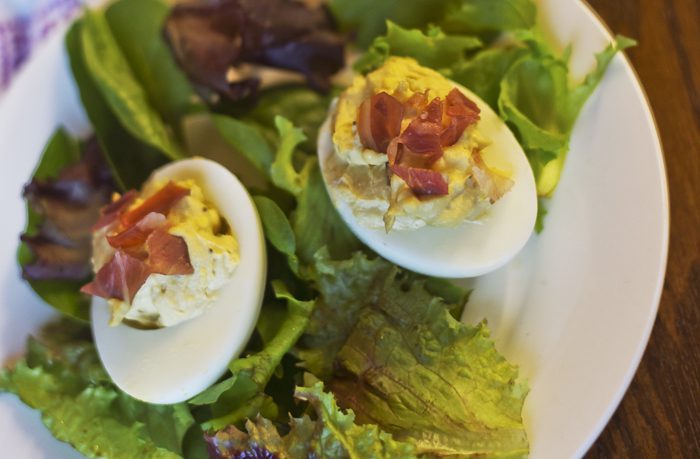 A plate holds a salad with mixed greens, snap peas, and deviled eggs topped with bacon.