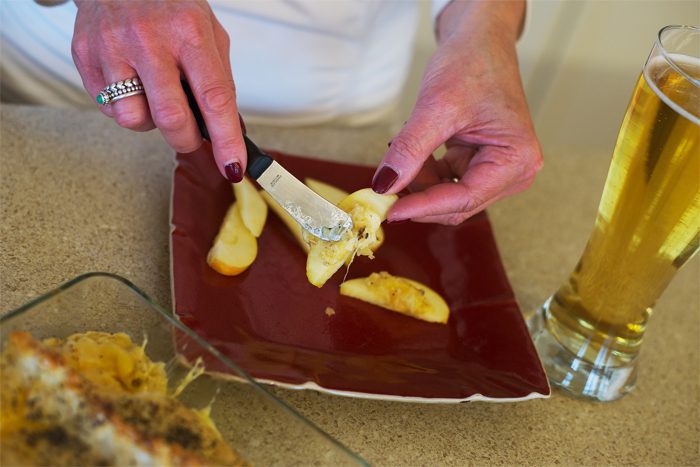 A person spreads soft cheese on bread with a glass of beer nearby.