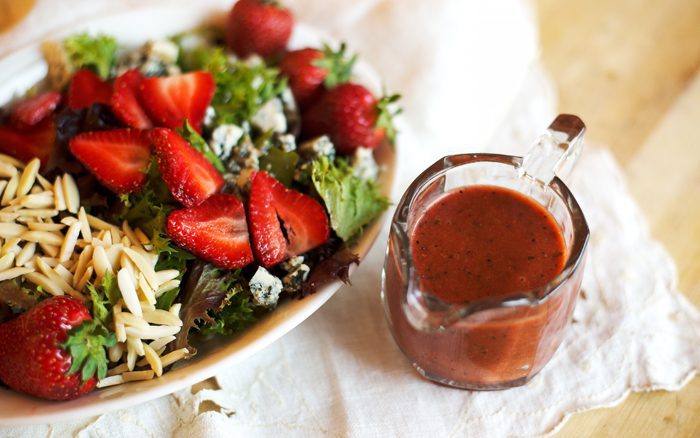 A fresh salad topped with strawberries and cheese next to a jar of dressing.