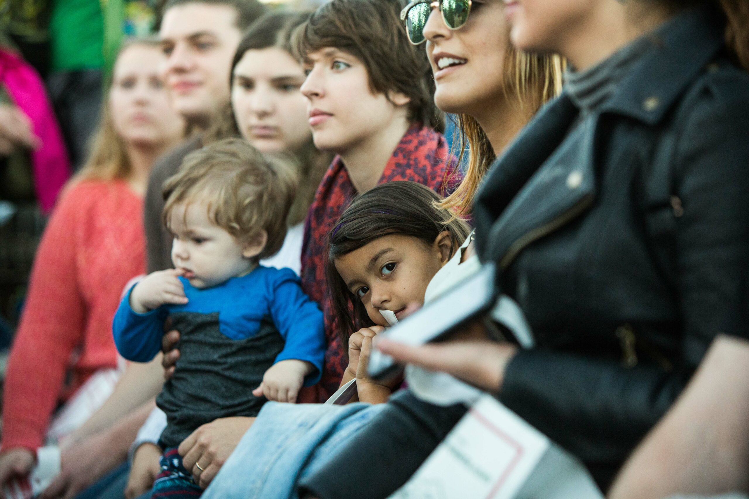 A diverse group of individuals is attentively watching an event, including a child on one person's lap.