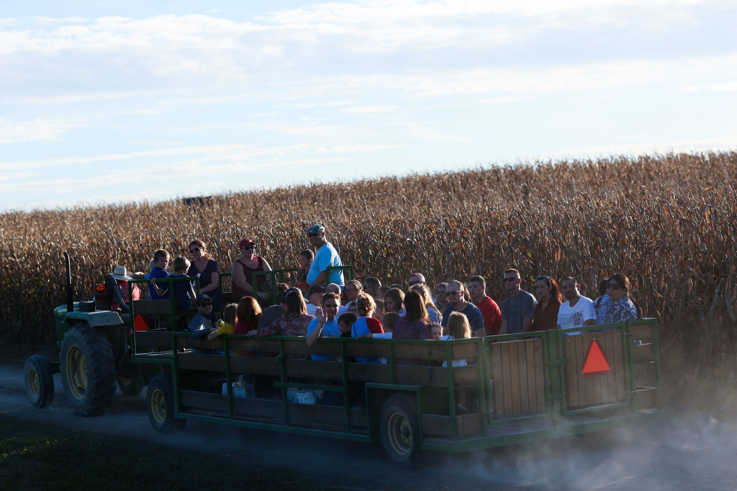A tractor pulls a wagon full of passengers through a cornfield under a clear sky.