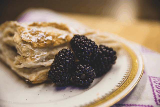 A flaky pastry topped with powdered sugar accompanied by juicy blackberries on a decorative plate.