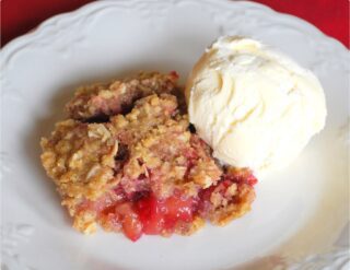 A serving of apple crumble with a scoop of vanilla ice cream on a white plate.