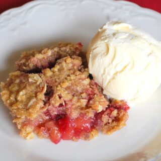 A serving of apple crumble with a scoop of vanilla ice cream on a white plate.