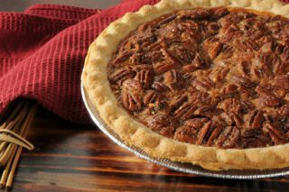 A freshly baked pecan pie sits on a wooden table next to cinnamon sticks and a red cloth.