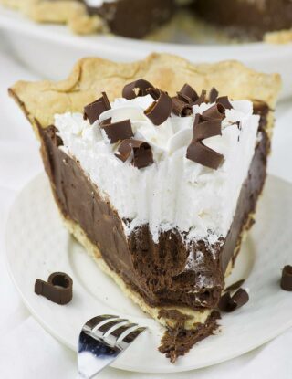 A slice of chocolate pie topped with whipped cream and chocolate shavings is served on a white plate.