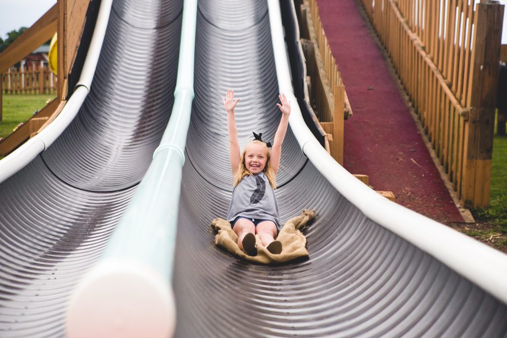 A joyful child slides down a dual metal slide with hands raised in excitement.