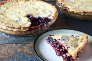 A freshly baked berry pie with a slice on a plate revealing a juicy filling.