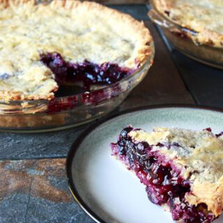 A freshly baked berry pie with a slice on a plate revealing a juicy filling.