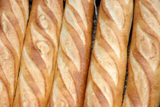 Rows of fresh, golden-brown baguettes with a traditional pattern of diagonal slashes.