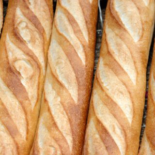 Rows of fresh, golden-brown baguettes with a traditional pattern of diagonal slashes.