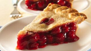 A slice of cherry pie with a flaky crust and vibrant filling is served on a white plate.