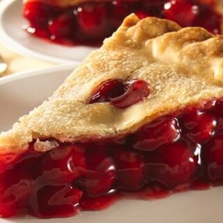 A slice of cherry pie with a flaky crust and vibrant filling is served on a white plate.