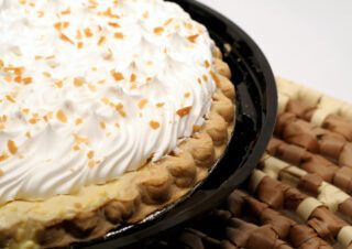 A close-up of a cream-topped pie sprinkled with chopped nuts in a black dish.