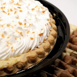 A close-up of a cream-topped pie sprinkled with chopped nuts in a black dish.