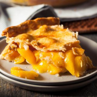 A slice of peach pie with a flaky crust on a plate, demonstrating a delicious homemade dessert.