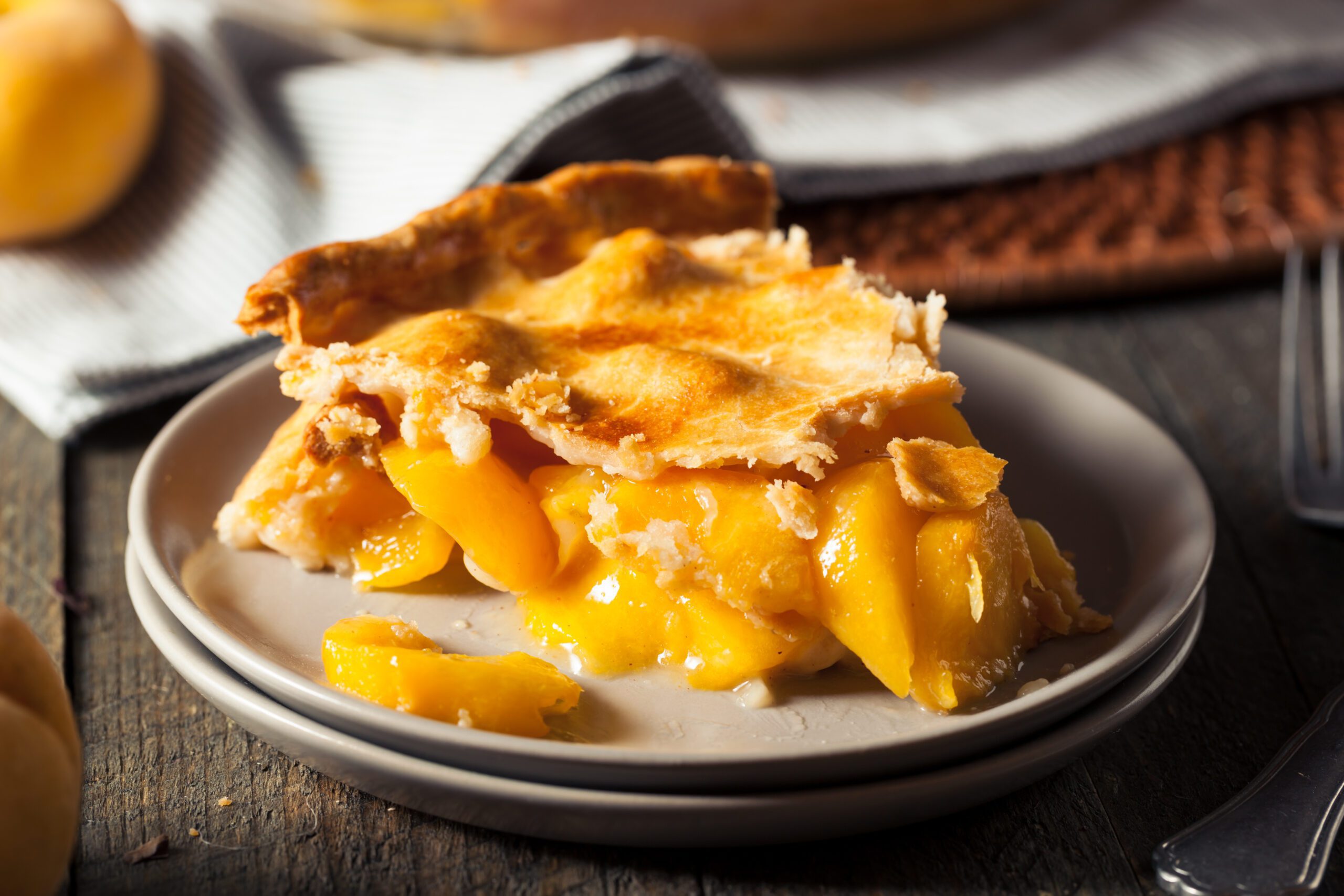 A slice of peach pie with a flaky crust on a plate, demonstrating a delicious homemade dessert.