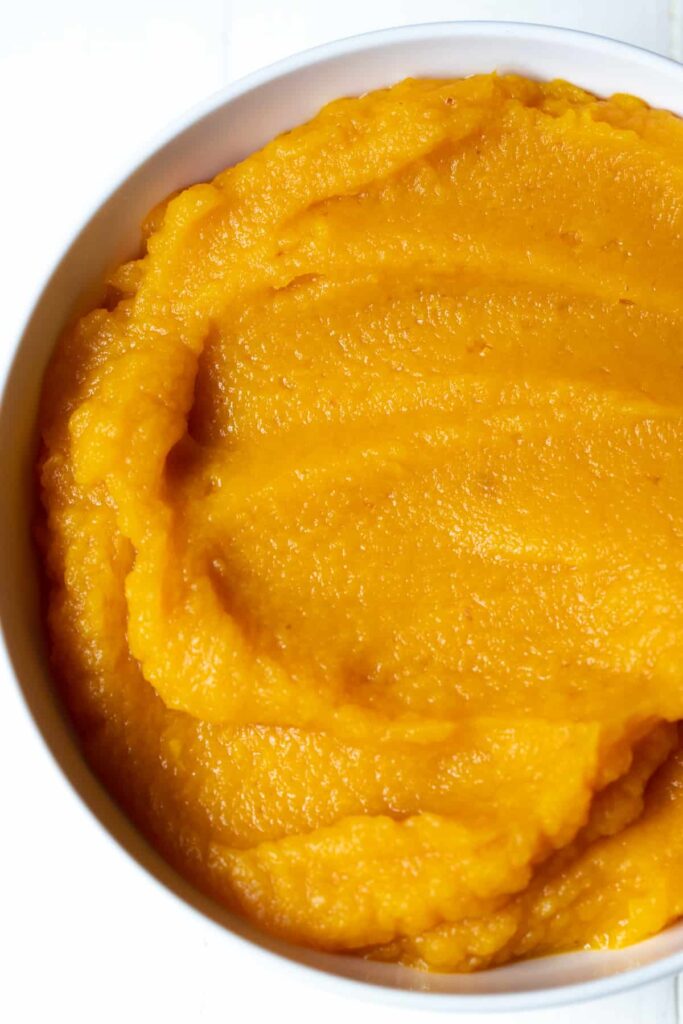 A bowl of smooth, orange-colored mashed sweet potatoes is presented on a white background.