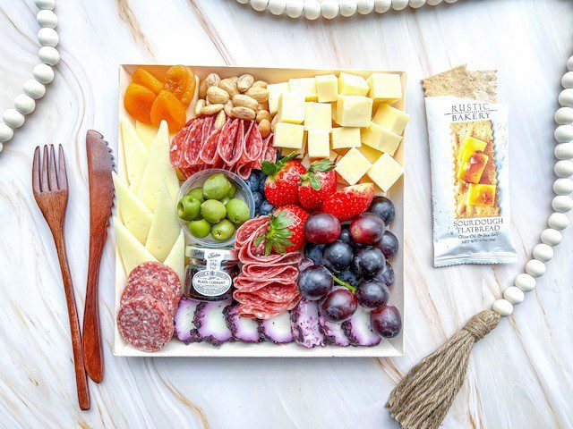 A charcuterie board filled with an assortment of cheeses, meats, fruits, nuts, and crackers with utensils on the side.