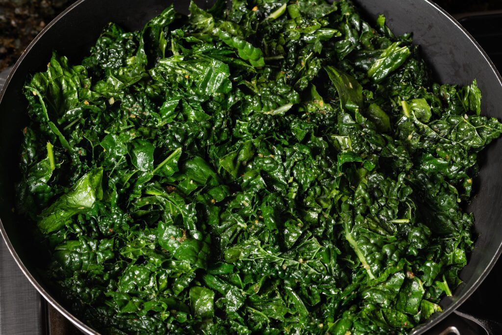 A pan full of sautéed dark green, leafy kale glistening with oil over a stove.