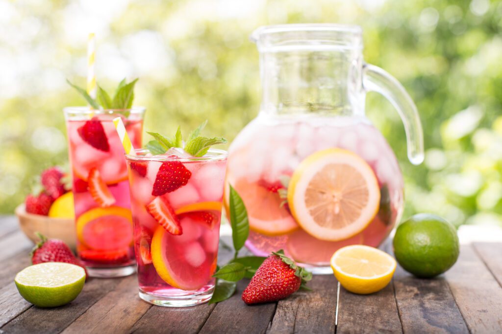 A refreshing pitcher of fruit-infused water with matching glasses garnished with strawberries and mint on a sunny table.