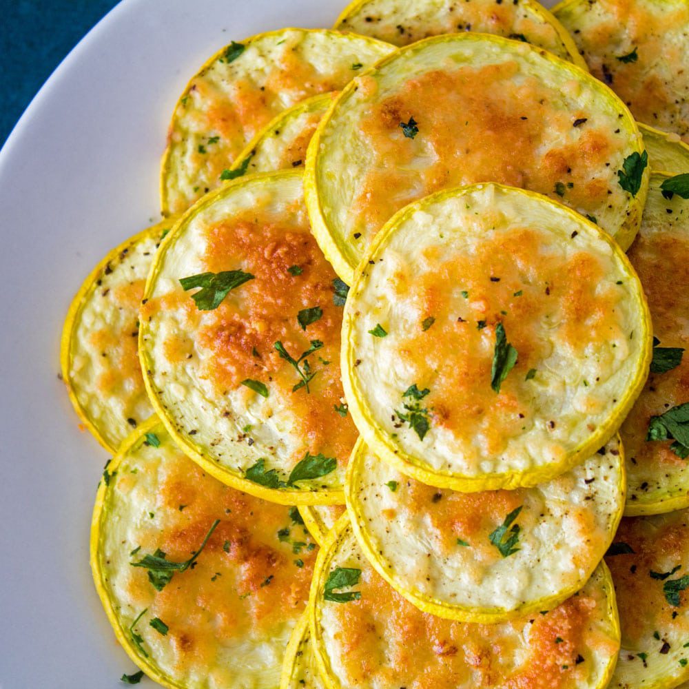 A plate of baked seasoned zucchini slices topped with melted cheese and herbs.