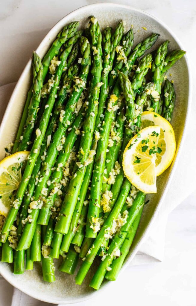 A plate of cooked asparagus garnished with lemon slices and herbs.